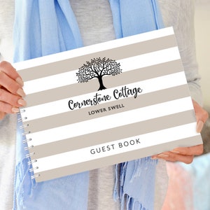以下が含まれることがあります： 白とグレーのストライプのゲストブック。黒い木のシルエットと「Cornerstone Cottage Lower Swell Guest Book」の文字が書かれています。
