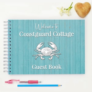Könnte beinhalten: Ein blaues und weißes Gästebuch mit einer Krabbenillustration und dem Text "Willkommen im Coastguard Cottage Gästebuch".