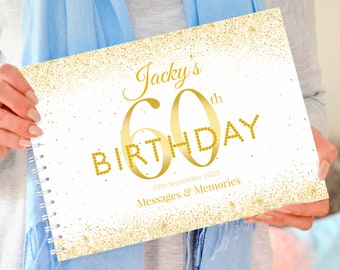 May include: A spiral-bound guest book with a white cover featuring gold glitter accents and the text Jacky's 60th BIRTHDAY 30th September 2023 Messages & Memories. The design includes a large gold number 60 and gold dot lettering.