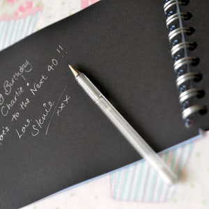 May include: A black notebook with a silver pen and a handwritten message that says "Happy Birthday Charlie! Here's to the Next 40!! Love, Stevie xxx".