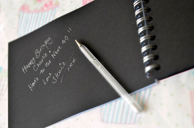 May include: A black notebook with a silver pen and a handwritten message that says "Happy Birthday Charlie! Here's to the Next 40!! Love, Stevie xxx".