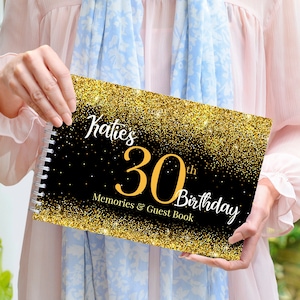 Può includere: Un libro degli ospiti per il 30° compleanno nero e oro con il nome "Katie's" in corsivo bianco. La copertina presenta accenti glitterati dorati e le parole "Memories & Guest Book". Il libro è rilegato a spirale.
