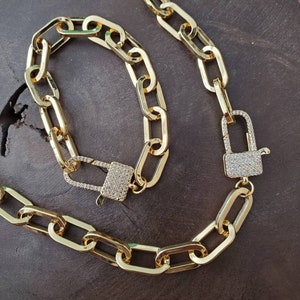 May include: A gold chain necklace and bracelet set with a padlock clasp. Both pieces are adorned with clear cubic zirconia stones.