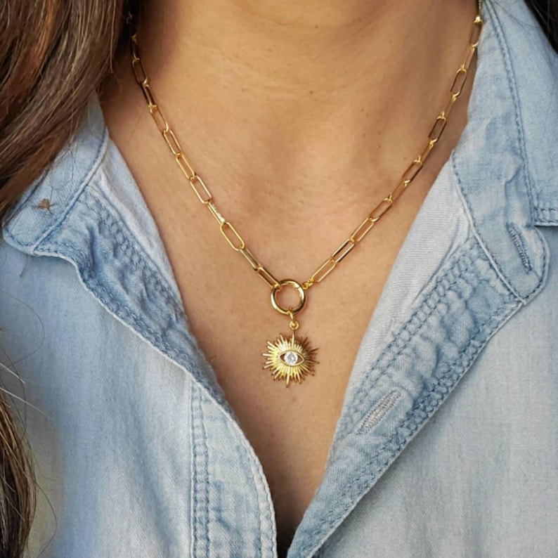 May include: Gold chain necklace with a gold sun charm featuring a white evil eye in the center.