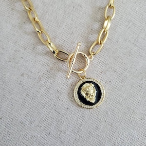 May include: A gold chain necklace with a toggle clasp and a round pendant featuring a lion head design with black enamel and clear rhinestones.