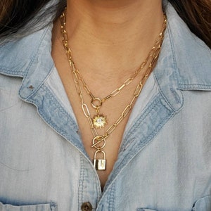 May include: Gold chain necklace with a gold evil eye charm and a gold padlock charm.