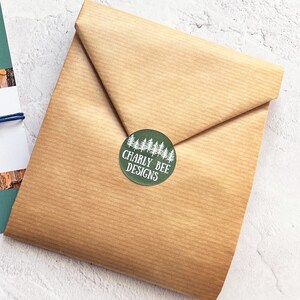 Puede incluir: Un paquete envuelto en papel marr&oacute;n, sellado con una pegatina redonda verde. La pegatina presenta un dise&ntilde;o de &aacute;rboles blancos y el texto "Charly Bee Designs". El papel est&aacute; doblado.