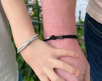 Puede incluir: Dos pulseras a juego. Una es azul claro con un dije cuadrado plateado con la letra "N". La otra es negra con un dije cuadrado plateado con la letra "E". Las pulseras se llevan en las muñecas.