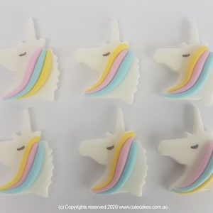 May include: Six white unicorn head cake toppers with pastel pink, yellow, and blue rainbow manes.