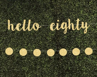 May include: Gold glitter banner with the text "hello eighty" and a string of gold glitter circles.
