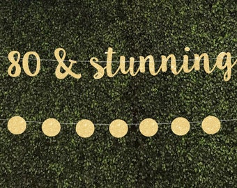 May include: Gold glitter banner with the text "80 & stunning" and a string of gold glitter circles.