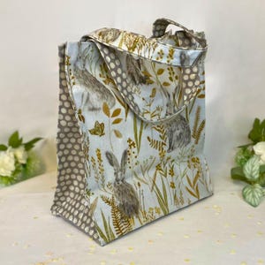 Peut inclure: Un sac fourre-tout en tissu avec un fond bleu clair orn&eacute; de li&egrave;vres, de plantes et de papillons. Les c&ocirc;t&eacute;s et les poign&eacute;es pr&eacute;sentent un motif &agrave; pois gris. Ce sac est con&ccedil;u pour transporter des objets.