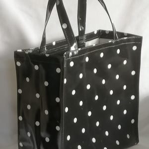 Könnte beinhalten: Eine schwarze Tragetasche mit weißen Punkten. Die Tasche hat zwei Henkel und einen Reißverschluss.