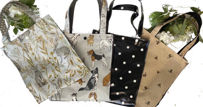 Peut inclure: Quatre sacs fourre-tout avec diff&eacute;rents motifs. L'un pr&eacute;sente un motif de lapin et de plantes sur fond clair. Un autre a un motif de chien. Le troisi&egrave;me sac est noir avec des pois blancs. Le dernier sac est beige avec un motif d'abeilles.