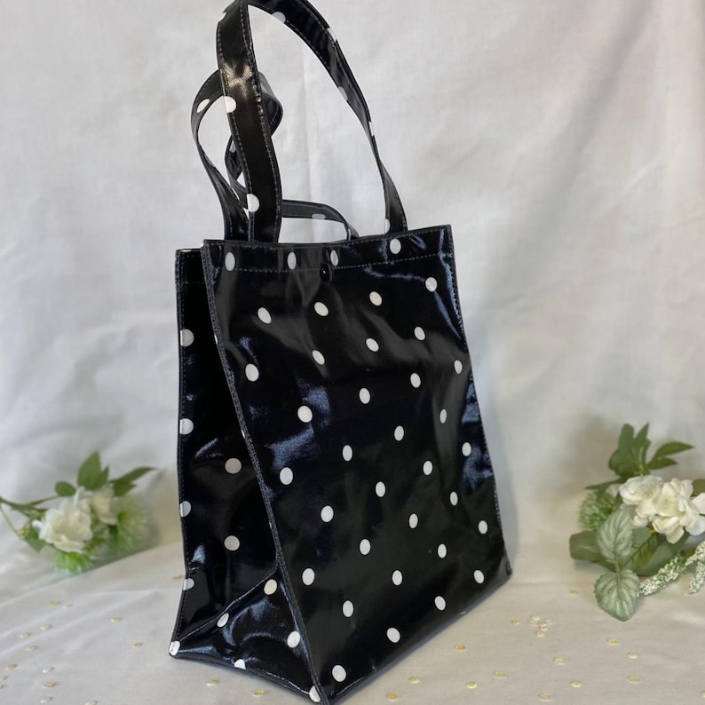 Peut inclure: Sac fourre-tout noir &agrave; pois blancs. Le sac a deux poign&eacute;es et une finition brillante. Le sac est rectangulaire avec un fond plat et convient au transport de divers articles.