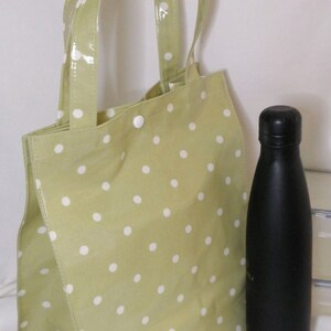 Peut inclure: Un sac fourre-tout vert clair &agrave; pois blancs et une bouteille d'eau noire. Le sac fourre-tout a deux poign&eacute;es et est fait d'un mat&eacute;riau brillant. La bouteille d'eau est haute et &eacute;lanc&eacute;e avec un bouchon noir.