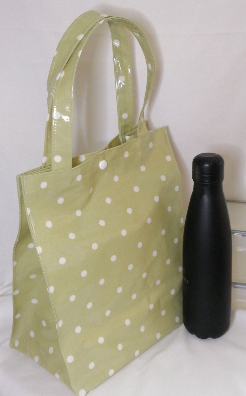 Peut inclure: Un sac fourre-tout vert clair &agrave; pois blancs et une bouteille d'eau noire. Le sac fourre-tout a deux poign&eacute;es et est fait d'un mat&eacute;riau brillant. La bouteille d'eau est haute et &eacute;lanc&eacute;e avec un bouchon noir.