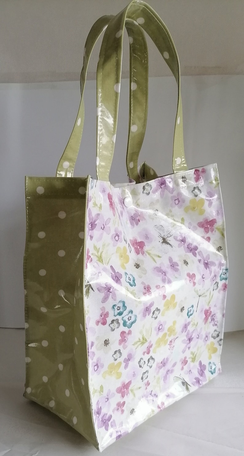 Peut inclure: Un sac fourre-tout &agrave; motifs floraux et &agrave; pois verts. Le sac pr&eacute;sente un fond blanc avec des fleurs violettes, roses et jaunes. Les poign&eacute;es et un c&ocirc;t&eacute; du sac sont vert olive avec des pois blancs. Fermeture &agrave; bouton-pression blanche.