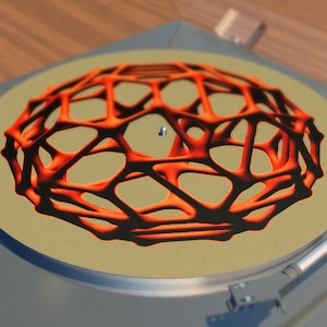 Pode incluir: Um toca-discos com uma esteira deslizante bege com um design geométrico vermelho e preto. O design se assemelha a uma esfera 3D com uma estrutura de arame.