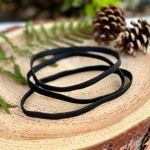 Op de afbeelding: Drie zwarte elastische haarbandjes op een houten oppervlak. De haarbandjes liggen op elkaar.