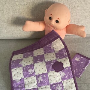 Puede incluir: Una colcha de retazos morada y blanca con dos aplicaciones de flores moradas. La colcha está hecha de cuadrados de tela con un patrón floral.
