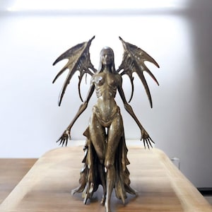 May include: A bronze sculpture of a skeletal figure with large, pointed wings. The figure has outstretched arms and is wearing a flowing garment. The sculpture is on a wooden surface.