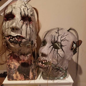 May include: Two creepy, realistic-looking masks with stitched mouths and cracked, painted faces. The masks are made of papier-m&acirc;ch&eacute; and have long, dark hair.