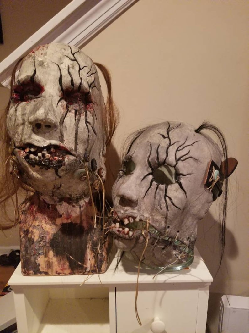 May include: Two creepy, realistic-looking masks with stitched mouths and cracked, painted faces. The masks are made of papier-m&acirc;ch&eacute; and have long, dark hair.