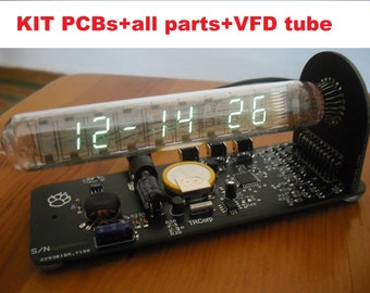 May include: A digital clock kit with a VFD tube displaying 12:14:26. The clock is built on a black circuit board with various electronic components. The text "KIT PCBs+all parts+VFD tube" is visible.