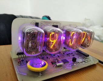 May include: A digital clock with four glowing Nixie tubes displaying the time. The tubes are encased in clear glass and emit an orange light. The clock's circuit board has various electronic components.
