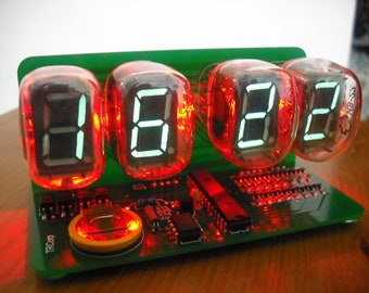 May include: A digital clock with four glowing orange Nixie tubes displaying the time 16:22. The clock is mounted on a green circuit board with various electronic components. The tubes are labeled "NB-55".