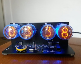 May include: A black digital clock with four glowing orange digits displayed in glass tubes. The tubes are surrounded by a blue light. The clock sits on a black base with electronic components.