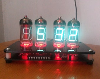 May include: A digital clock with four vacuum tubes displaying the time. The digits are illuminated in red and green against a black base. The clock has a retro, vintage aesthetic.