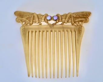 Puede incluir: Un peine para el cabello vintage de color marfil con un diseño decorativo de dos libélulas con acentos azul y morado iridiscentes. El peine tiene 12 dientes.