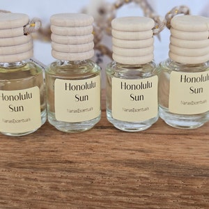 May include: Four small glass bottles with wooden caps and labels that read "Honolulu Sun" and "NanasEscentuals". The bottles are filled with a light-colored liquid and sit on a wooden surface.