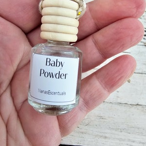 May include: A small glass bottle with a white label that reads "Baby Powder" and "NanasEscentials". The bottle has a wooden cap with a white bead and yellow string.
