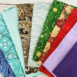 May include: A fan of assorted fabric swatches in various colors and patterns. Includes paisley, floral, and solid colors like blue, green, red, and purple. The fabrics are arranged on a light-colored wooden surface.