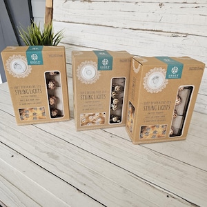 May include: Three rectangular cardboard boxes containing 10ft decorative LED string lights. Each box features a cutout window displaying the lights, with text reading 10ft decorative LED string lights, battery powered, and 10 warm white LED lights.