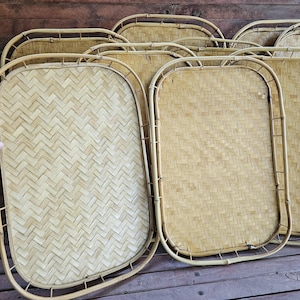 May include: A collection of woven bamboo trays with rounded edges. The trays have a light brown color and a textured surface. The trays are arranged on a wooden surface, showcasing their natural, rustic design. The trays are ideal for serving food or as decorative pieces.