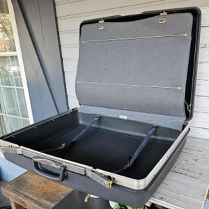May include: A black hard-sided suitcase with a gray fabric lining and a silver zipper. The suitcase is open and the interior is visible.