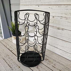 May include: Black metal coffee pod holder with a rotating base and a mesh design. The holder has a capacity of 36 pods and features a unique horseshoe-shaped design.