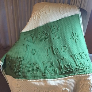 May include: A green and white crocheted baby blanket with the words "It's a Boy" in raised stitches.