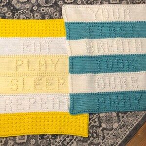 May include: Two crocheted baby blankets with different colors and text. The first blanket is yellow, white, and cream with the text "Eat, Play, Sleep, Repeat". The second blanket is teal, white, and cream with the text "Your First Breath Took Ours Away".
