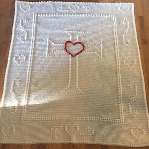 May include: A white crocheted blanket featuring a red heart at the centre of a white cross design.