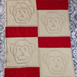 Könnte beinhalten: Eine gehäkelte Decke mit Patchwork-Muster. Die Decke ist aus beige und rotem Garn gefertigt und weist ein sich wiederholendes Muster aus Kreisen auf.