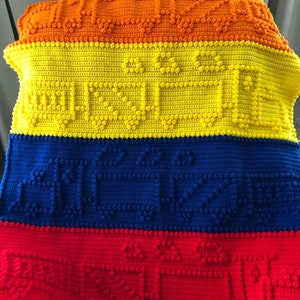 May include: A crocheted blanket with a multi-coloured striped pattern. The blanket is made of a textured yarn and has a raised design. The colours are orange, yellow, blue, and red.