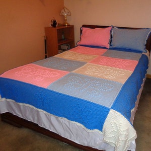 May include: A crocheted bedspread with a patchwork design featuring butterflies in shades of blue, pink, and white.