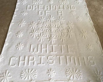 May include: White crochet blanket with the text "Dreaming of a White Christmas" in raised stitches. The blanket is decorated with snowflake designs.