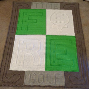May include: A crocheted blanket with a brown border and a green, white, and gray center. The center features the words "FORE" and "GOLF" in a stylized font.