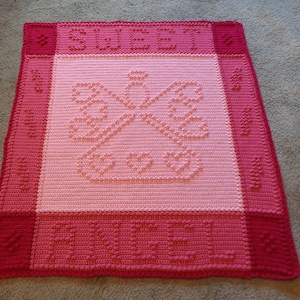 May include: A pink and red crocheted baby blanket with a heart design in the centre and the words "Sweet Dreams" at the top and "Love" at the bottom.